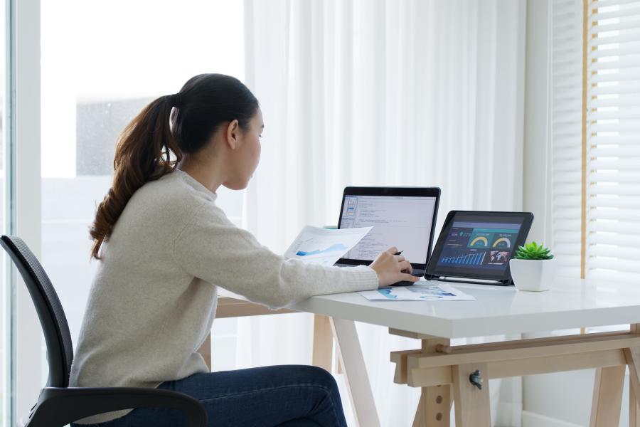 Woman working at desk with graphs on 2 screens